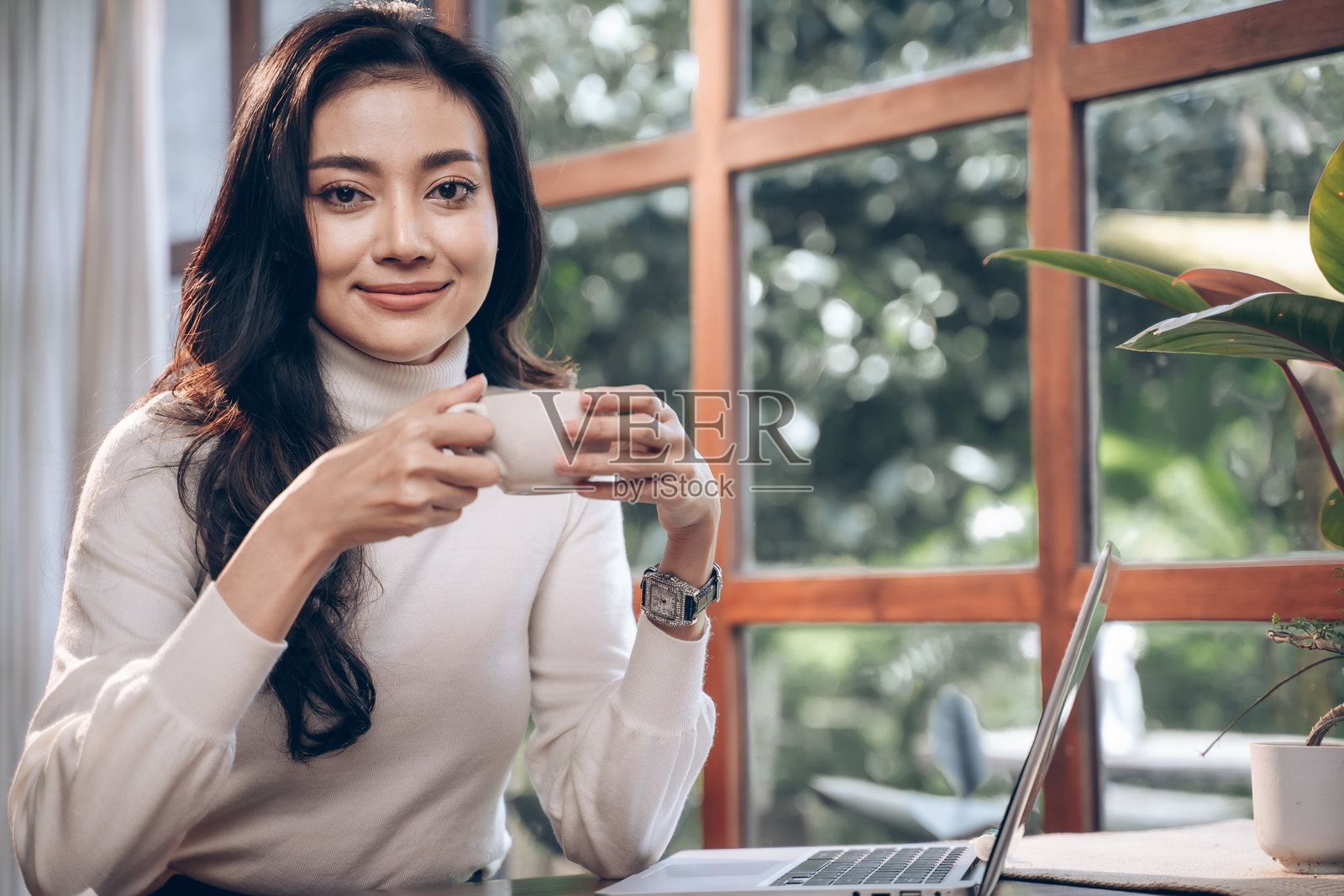 女商人在咖啡店里喝咖啡、使用智能手机，享受放松时光。年轻女性坐着，面带微笑，感到快乐。照片摄影图片