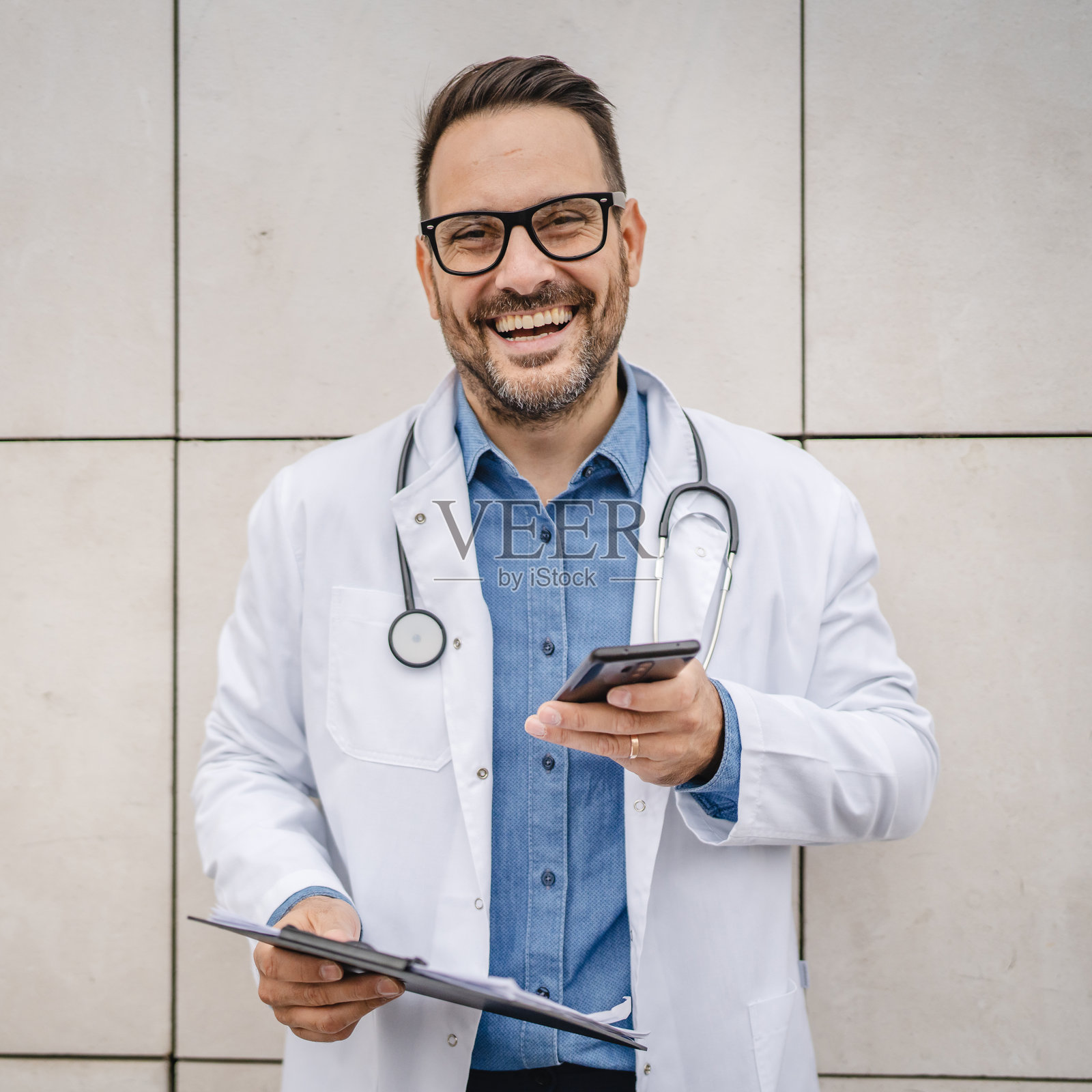 成年男性医生在白色墙壁前的咖啡休息时间使用手机照片摄影图片