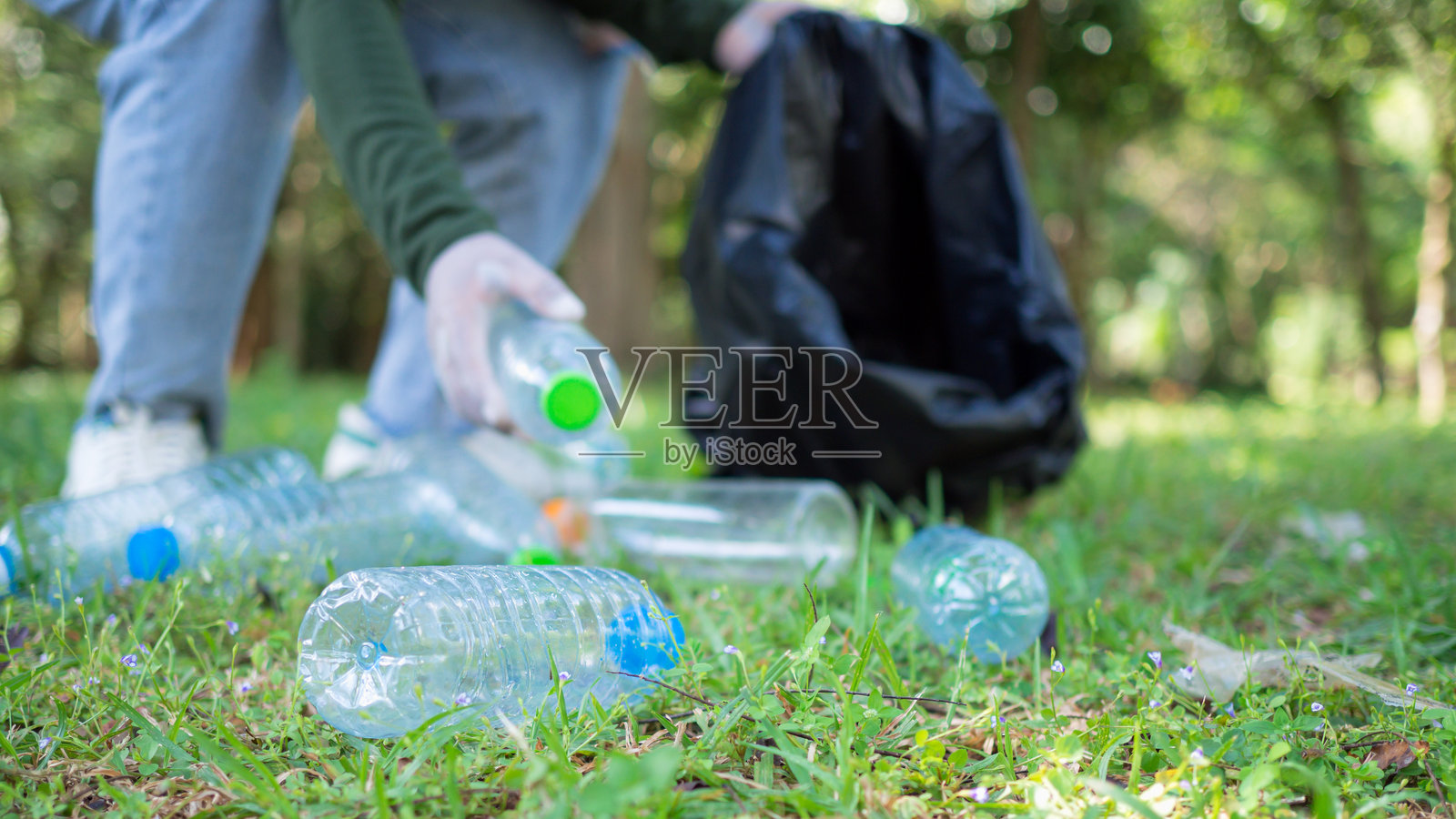 一群热心的女性志愿者正在公园参加环境清理活动。她们戴着手套，手里拿着大黑袋，正在收集公园里的垃圾和塑料瓶。照片摄影图片