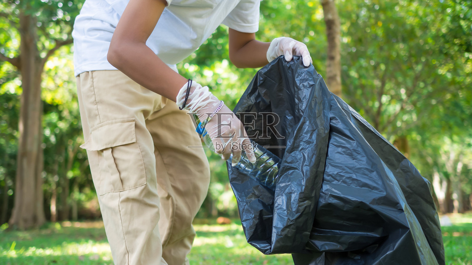 一群热心的志愿者正在公园参加环保清理活动。男孩戴着手套，手里拿着大黑袋子，正在公园里收集垃圾和塑料瓶。照片摄影图片