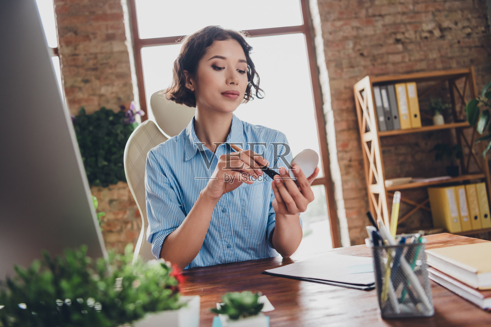 积极心态的女性专家穿着衬衫，在室内工作站上涂抹高光妆。照片摄影图片