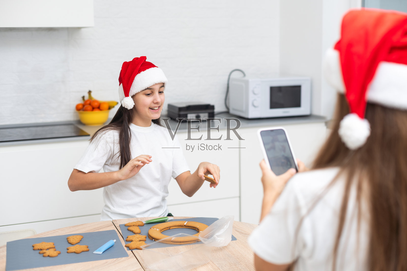 孩子们在温馨的家厨房里烘焙圣诞饼干。可爱的孩子们戴着圣诞老人帽为家人准备节日晚餐。姐妹们一起烤圣诞饼干。生活方式时刻。儿童厨师概念。照片摄影图片