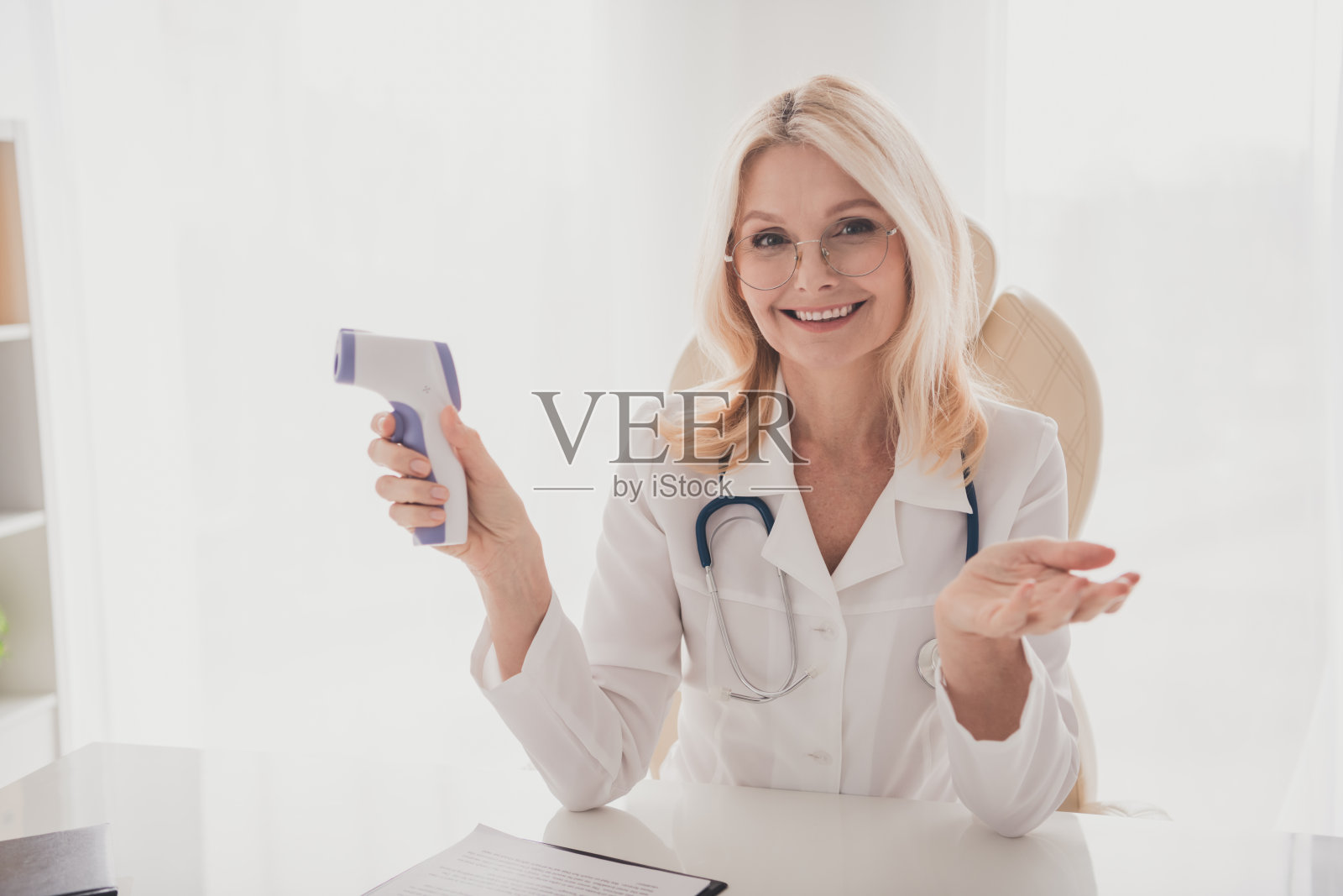 自信微笑的资深女医生在诊所办公室里手持医疗设备，准备进行病人咨询照片摄影图片