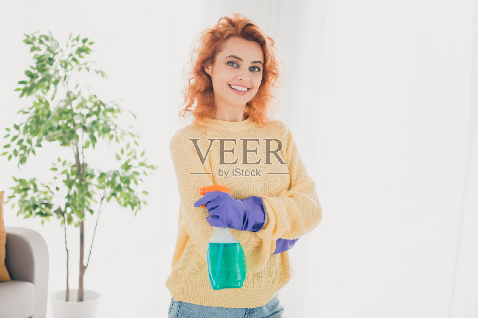 穿着黄色毛衣的积极心态女性在室内公寓房间里打扫卫生，手持喷雾器。照片摄影图片