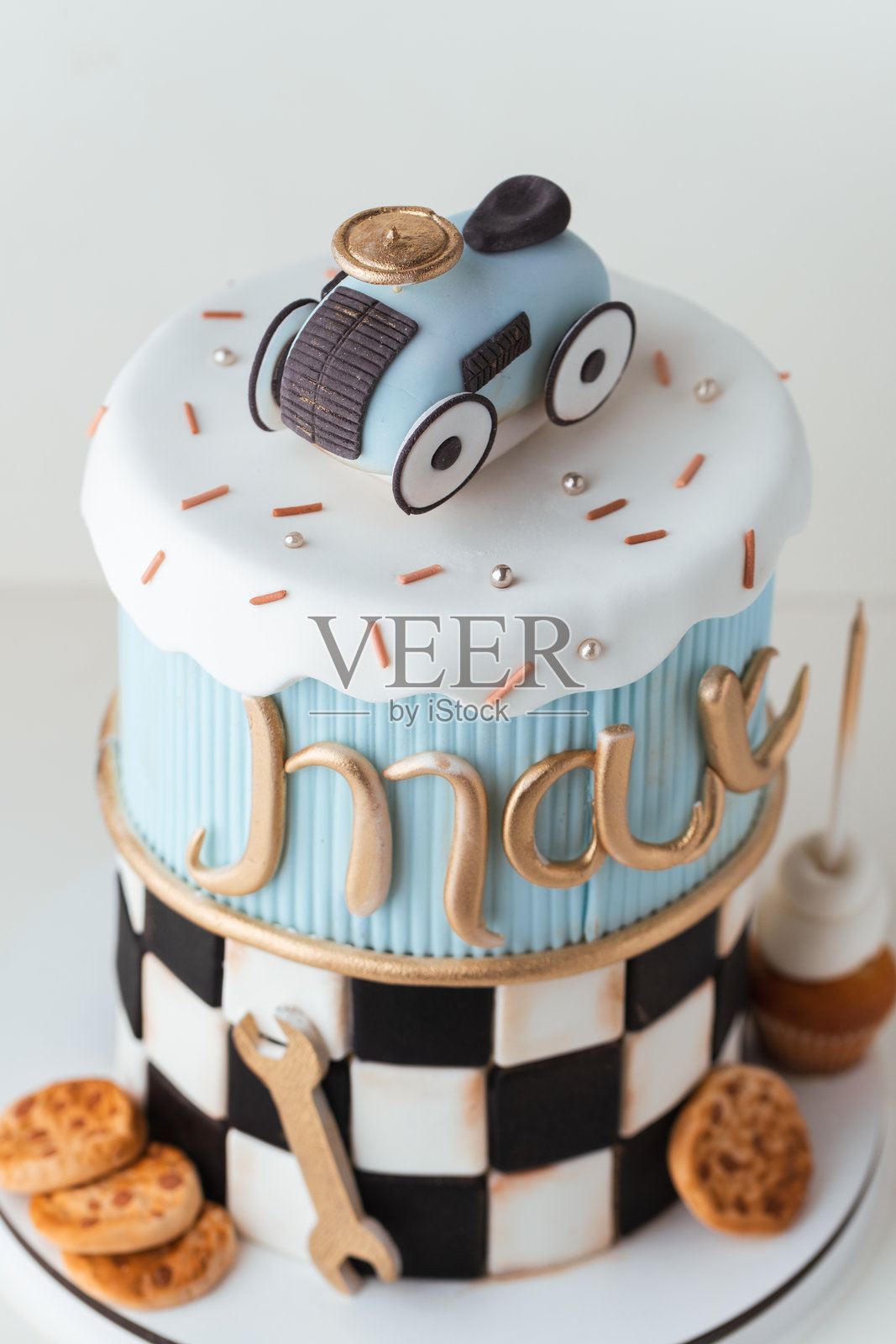美丽的高层双层翻糖蛋糕，背景为白色。为一个名叫马克斯的小男孩准备的生日蛋糕，顶部装饰有可食用的糖膏复古赛车和扳手。照片摄影图片