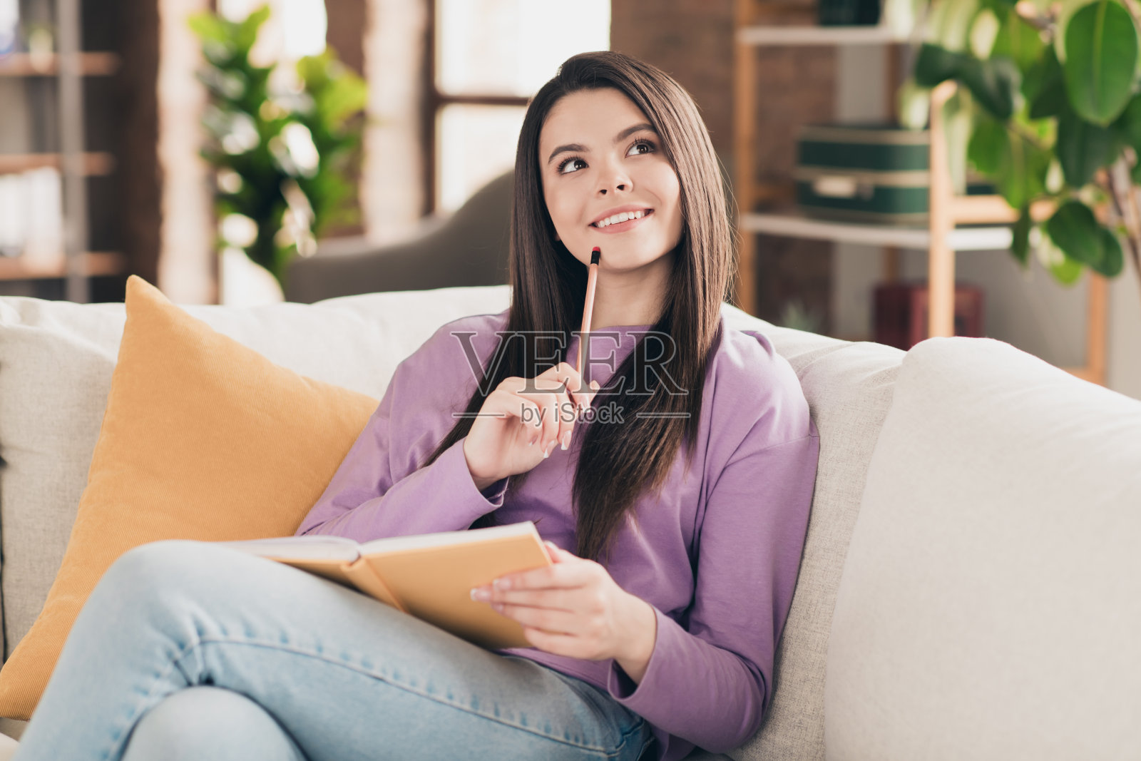 一位迷人的年轻少女穿着紫色服装，灵光一现地思考，正在阅读书籍，阳光明媚的舒适家庭室内客厅。照片摄影图片