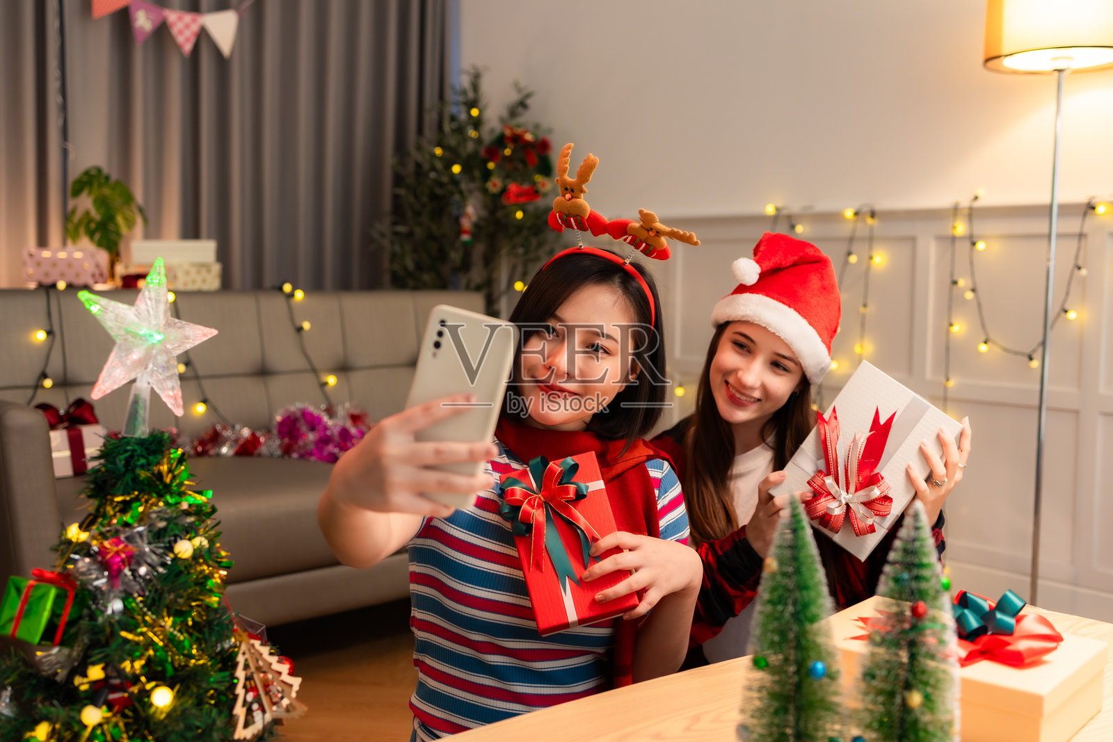 兴奋的亚洲女性在家中收到女友的惊喜礼物。赠送礼物。亚洲女性在圣诞节假期装饰圣诞树上的彩球。照片摄影图片