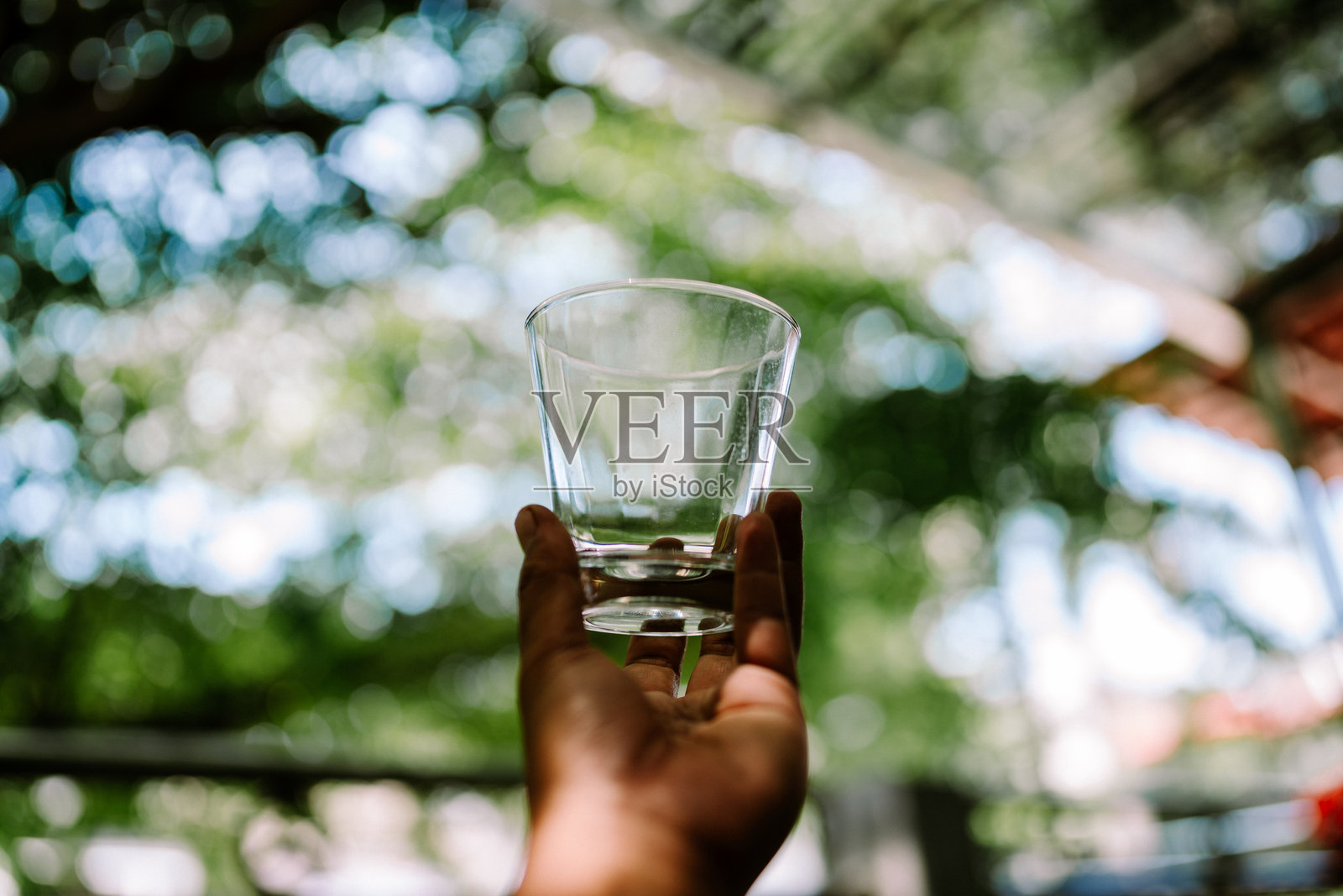 一只清澈的玻璃杯被手握住，捕捉光线的反射，展现其光滑的表面。照片摄影图片