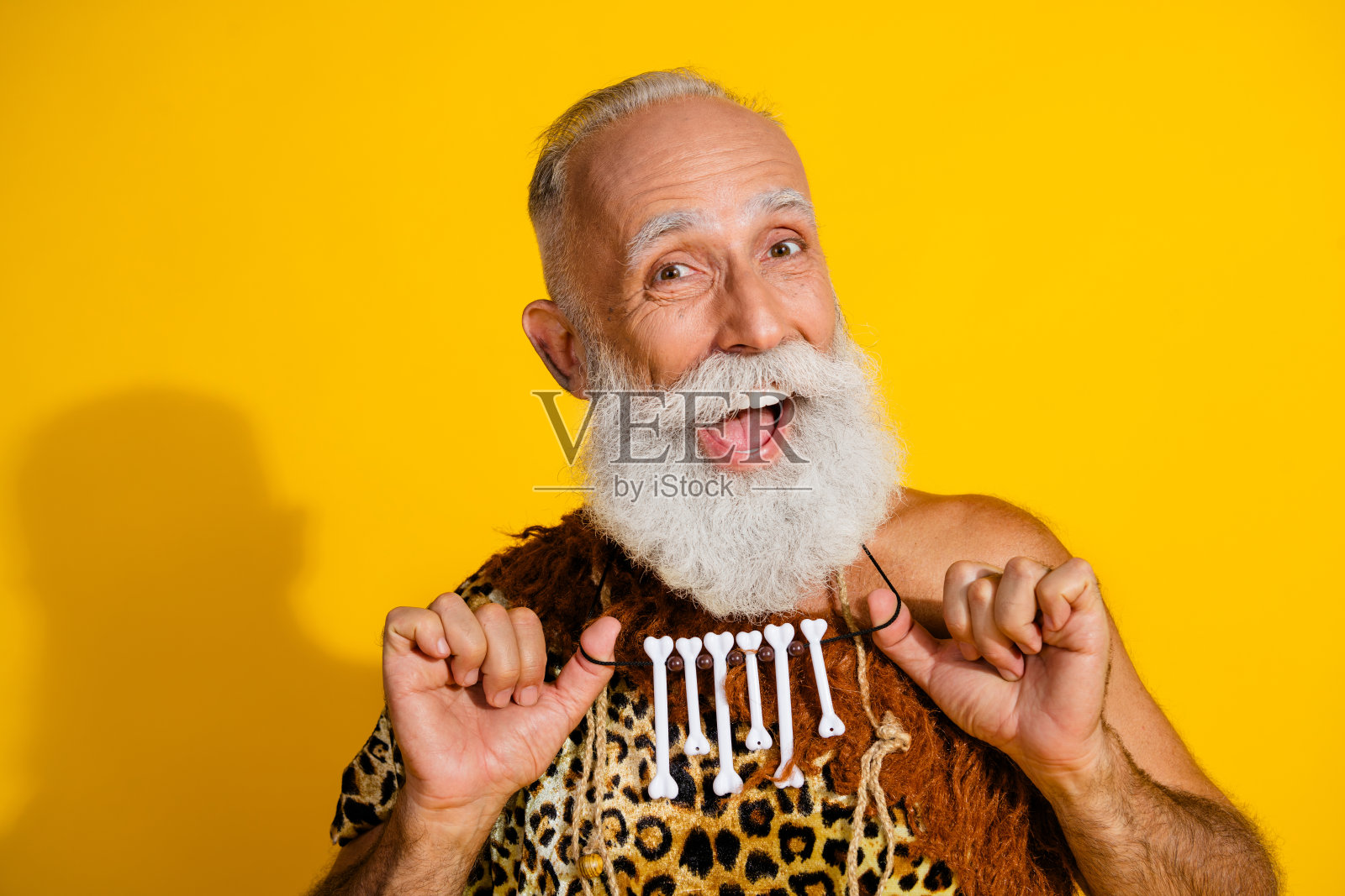 古老的穴居人照片，佩戴骨头项链，穿着豹纹衣服，背景为黄色。照片摄影图片