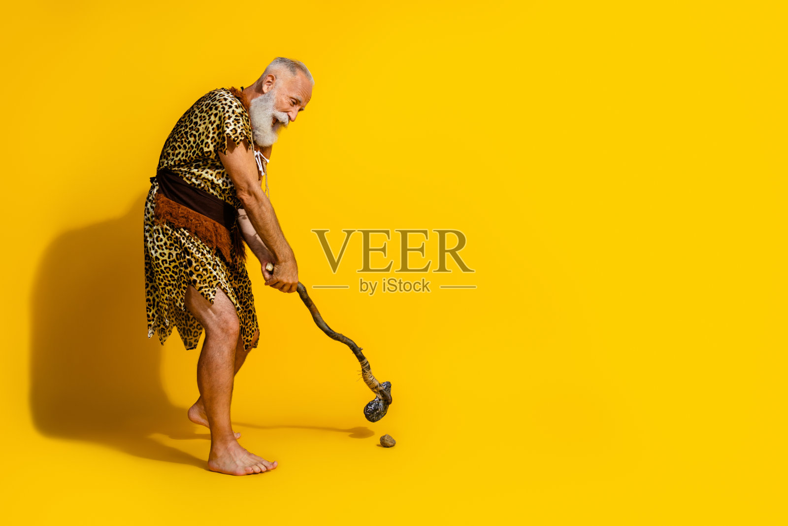 尼安德特人高尔夫球手侧面肖像，挥动石制球杆，背景为黄色。照片摄影图片