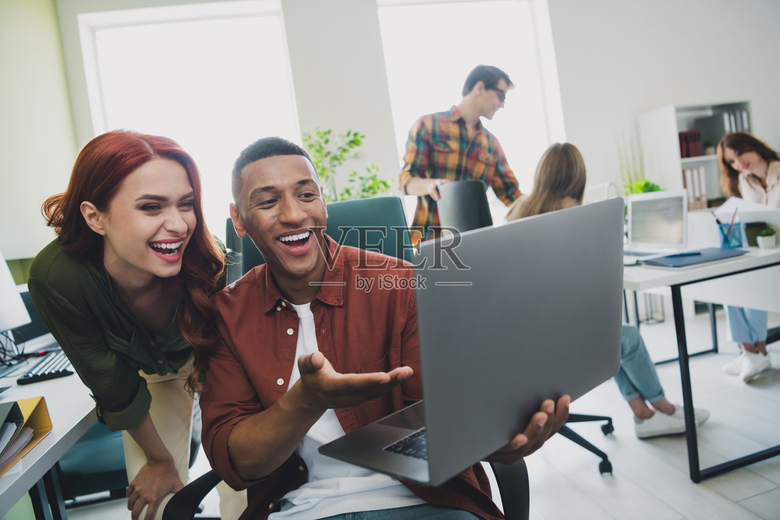 微笑的快乐网页设计师们在室内工作站一起合作，展示现代设备。照片摄影图片