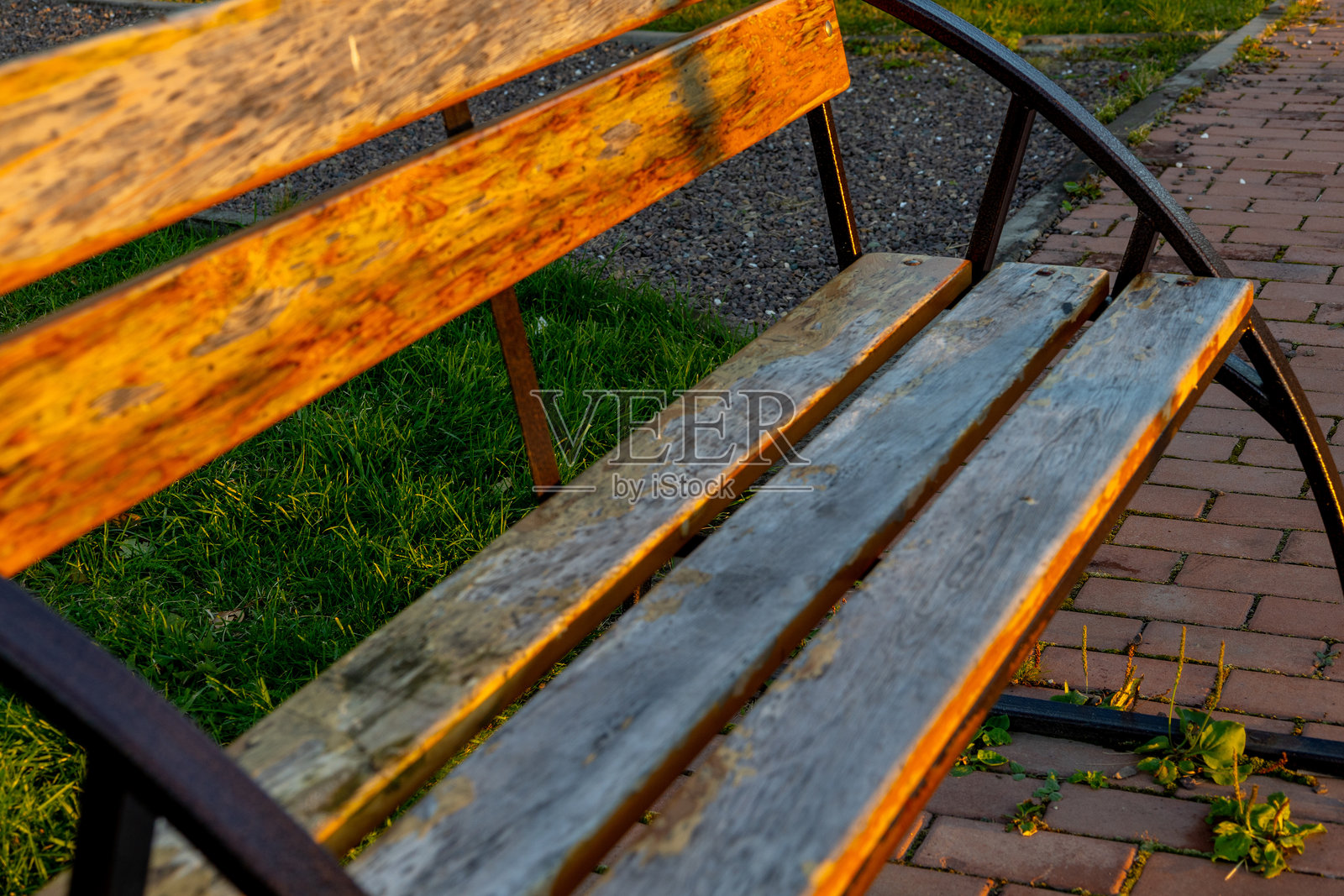 在宁静的公园环境中，温暖的阳光下，一张风化的木长椅静静地坐落于傍晚时分。照片摄影图片