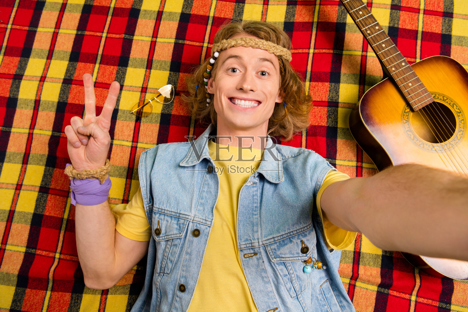 高角度视角的积极嬉皮士自拍，手指做出V字手势，躺在格子毯子上。照片摄影图片