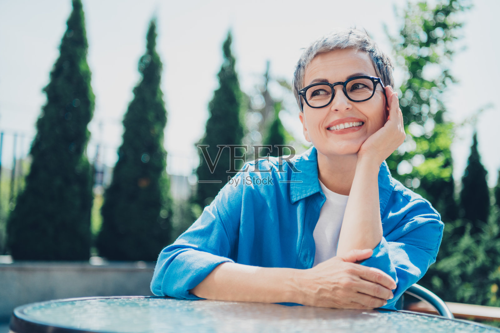 一位和蔼可亲的老年女士在市中心街头咖啡馆的户外桌子旁沉思，穿着蓝色衬衫。照片摄影图片