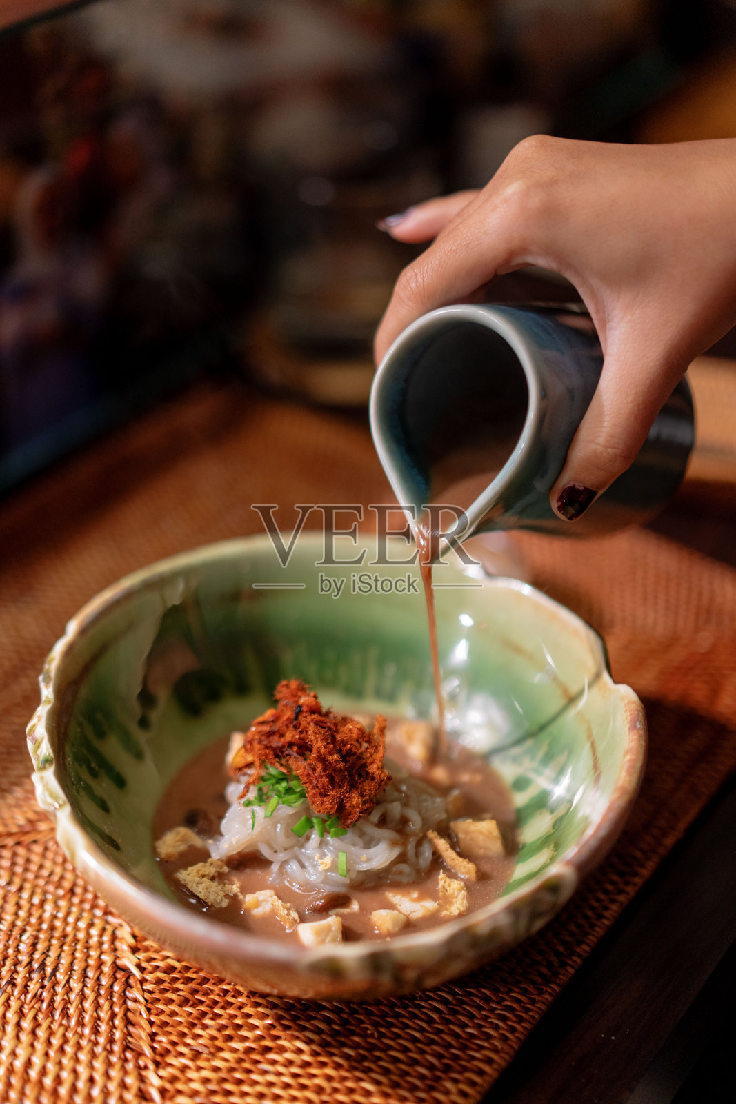 女性手部特写，将汤汁倒在当地美食印尼面条Mie Lethek上照片摄影图片