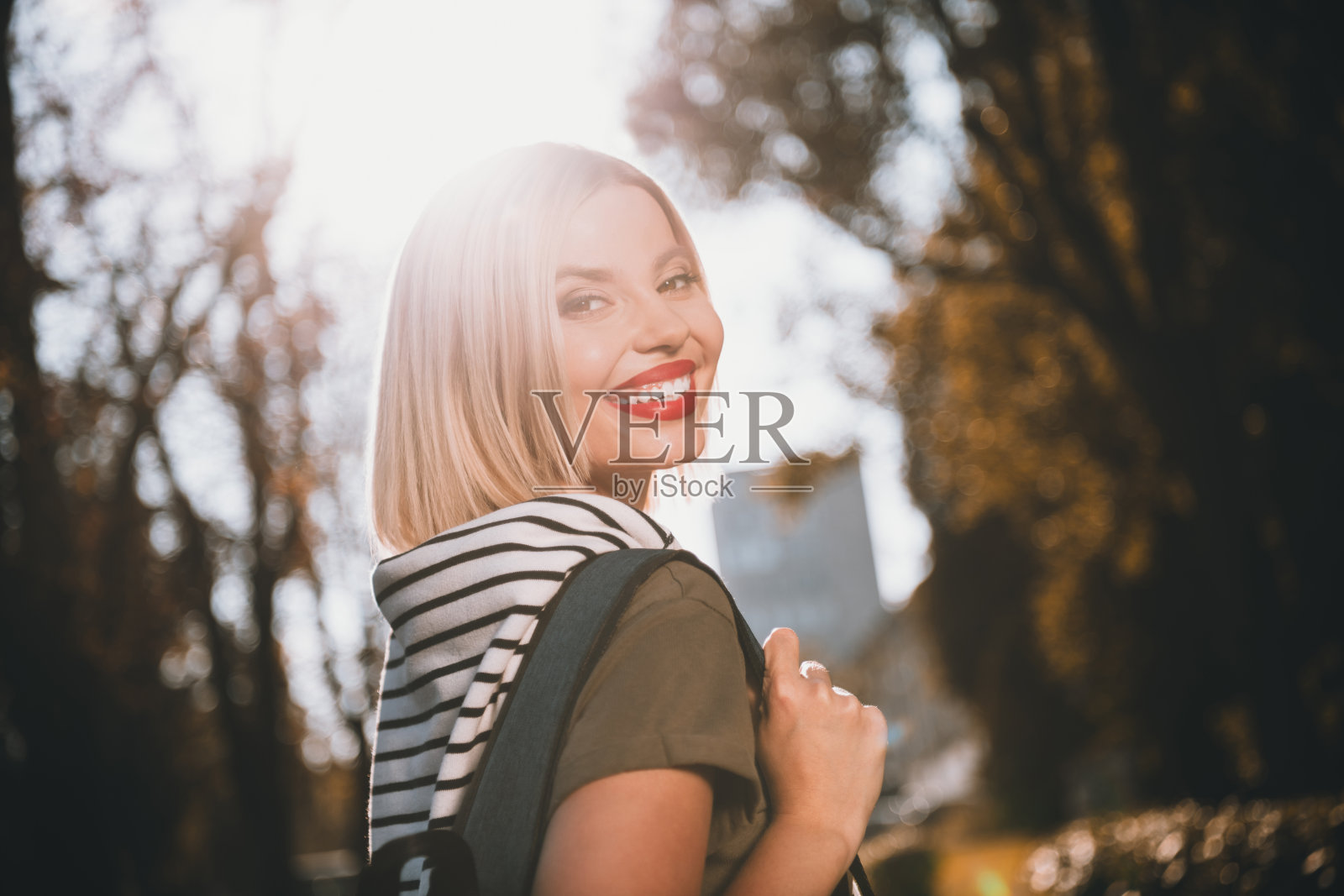 一位迷人的年轻女士在户外开心地微笑，穿着卡其色的肩带毛衣。照片摄影图片