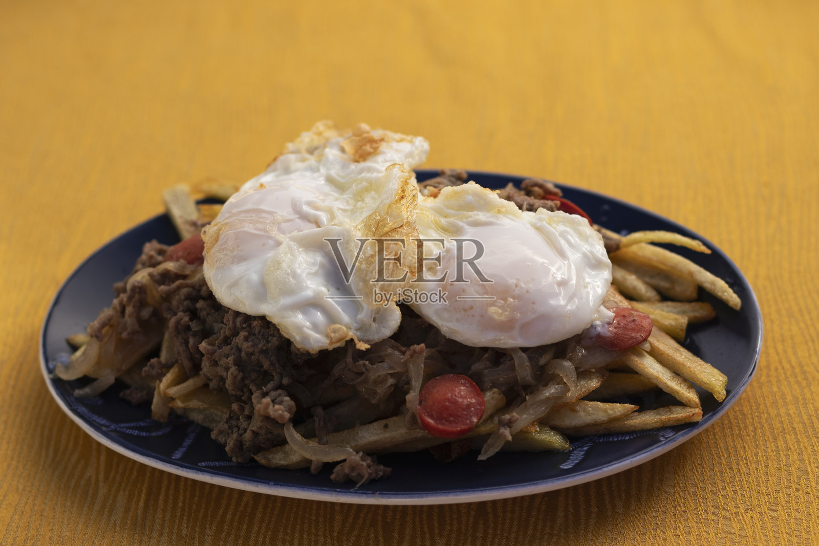 一盘撒盐的法式薯条，上面放有不同种类的切片肉、香肠、煎蛋和焦糖洋葱照片摄影图片
