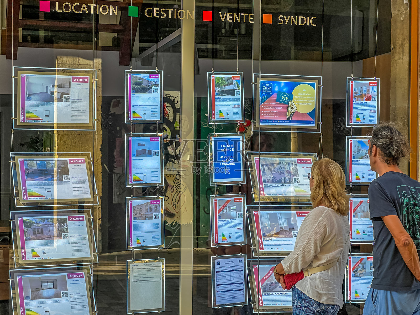 一对情侣在波尔多的房地产中介窗口查看房产广告。照片摄影图片