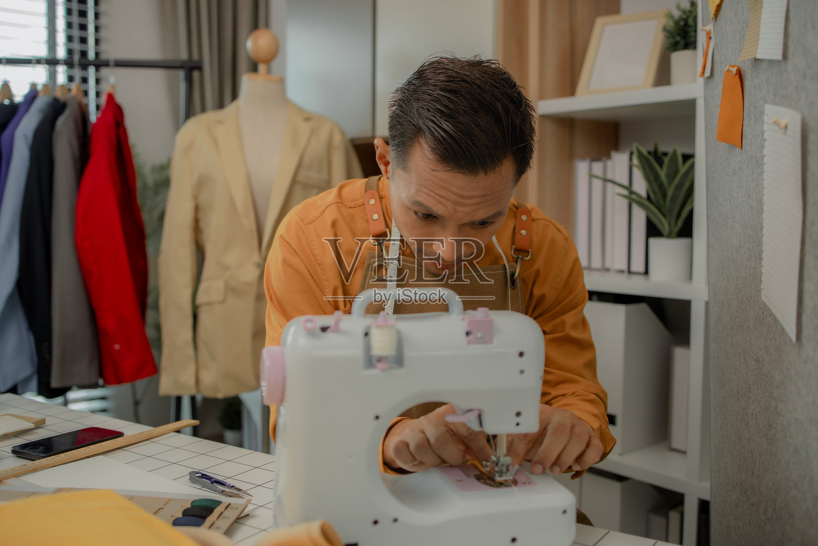 一位时装设计师在他的工作室里专注于自己热爱的工作，他做着许多事情，比如使用缝纫机缝制裙子，挑选制作裙子的面料。照片摄影图片