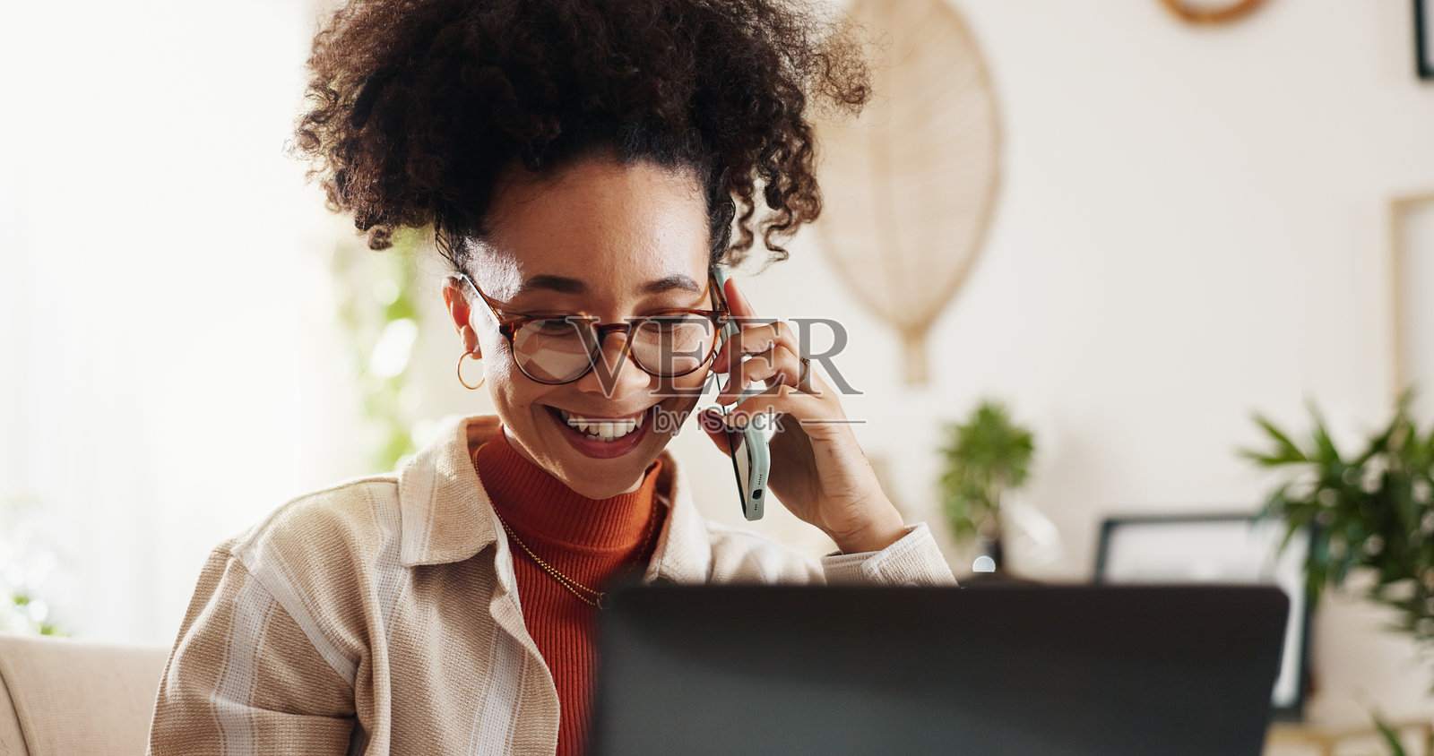 家中办公室的桌子上，有一位快乐的女性正在打电话，旁边放着笔记本电脑，适合用于沟通、日程安排或网络交流。远程工作、智能手机和顾问与联系、对话及自由职业的连接。照片摄影图片