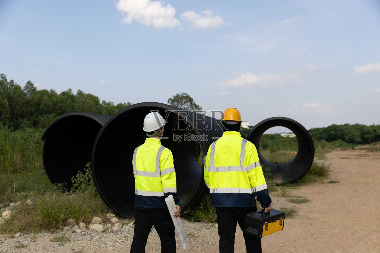两位年轻的土木工程师自信地在施工现场勘探，积极钻探道路以建立排水沟，阳光明媚的日子里，他们的专业知识确保了项目的高效进展和有效成果。照片摄影图片
