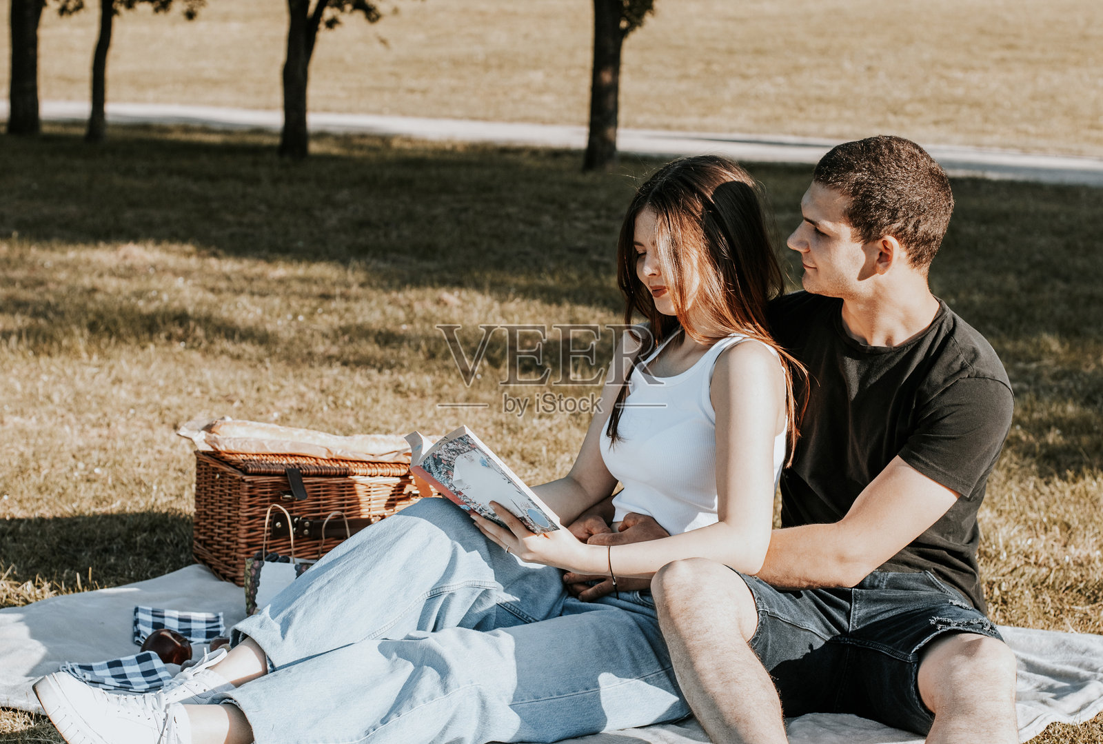 年轻情侣在公园野餐时阅读一本书。照片摄影图片