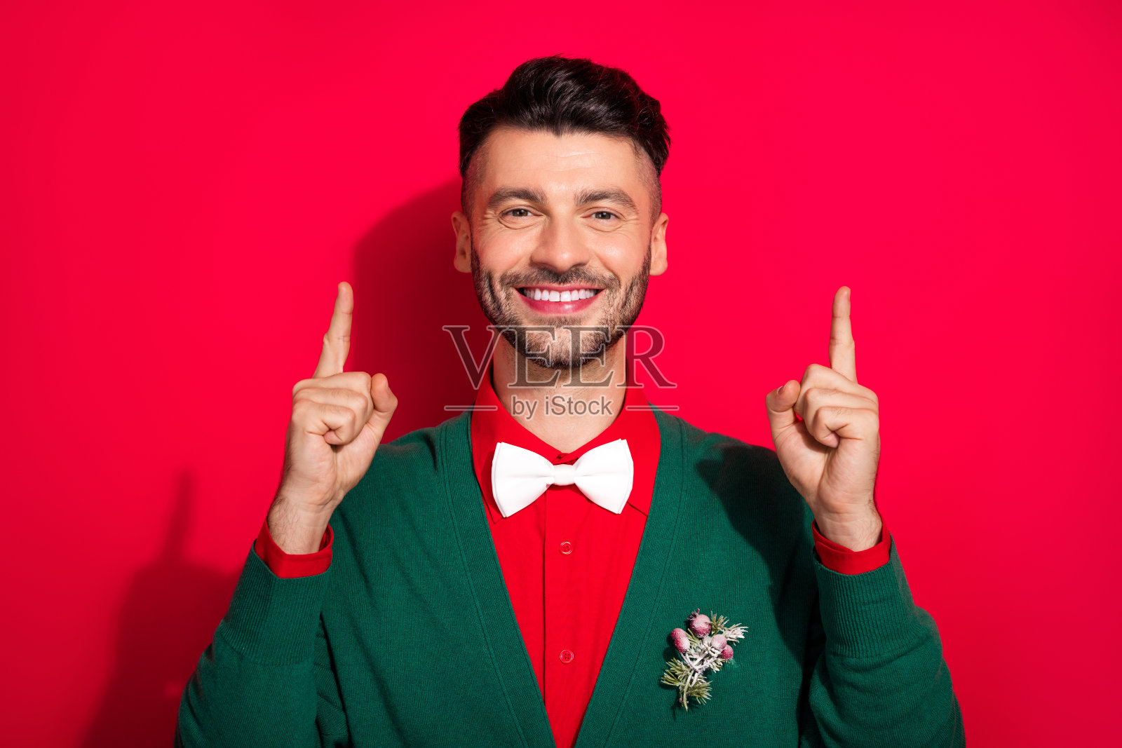 优雅的阳光男士微笑着，手指指向空旷的地方，背景为红色。照片摄影图片