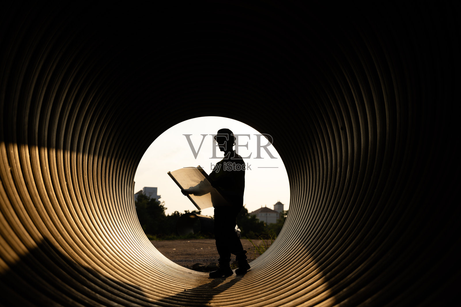 建筑工人和工程师在施工现场的大金属管道内高效工作。他们在傍晚日落前正在建设新的排水系统。照片摄影图片