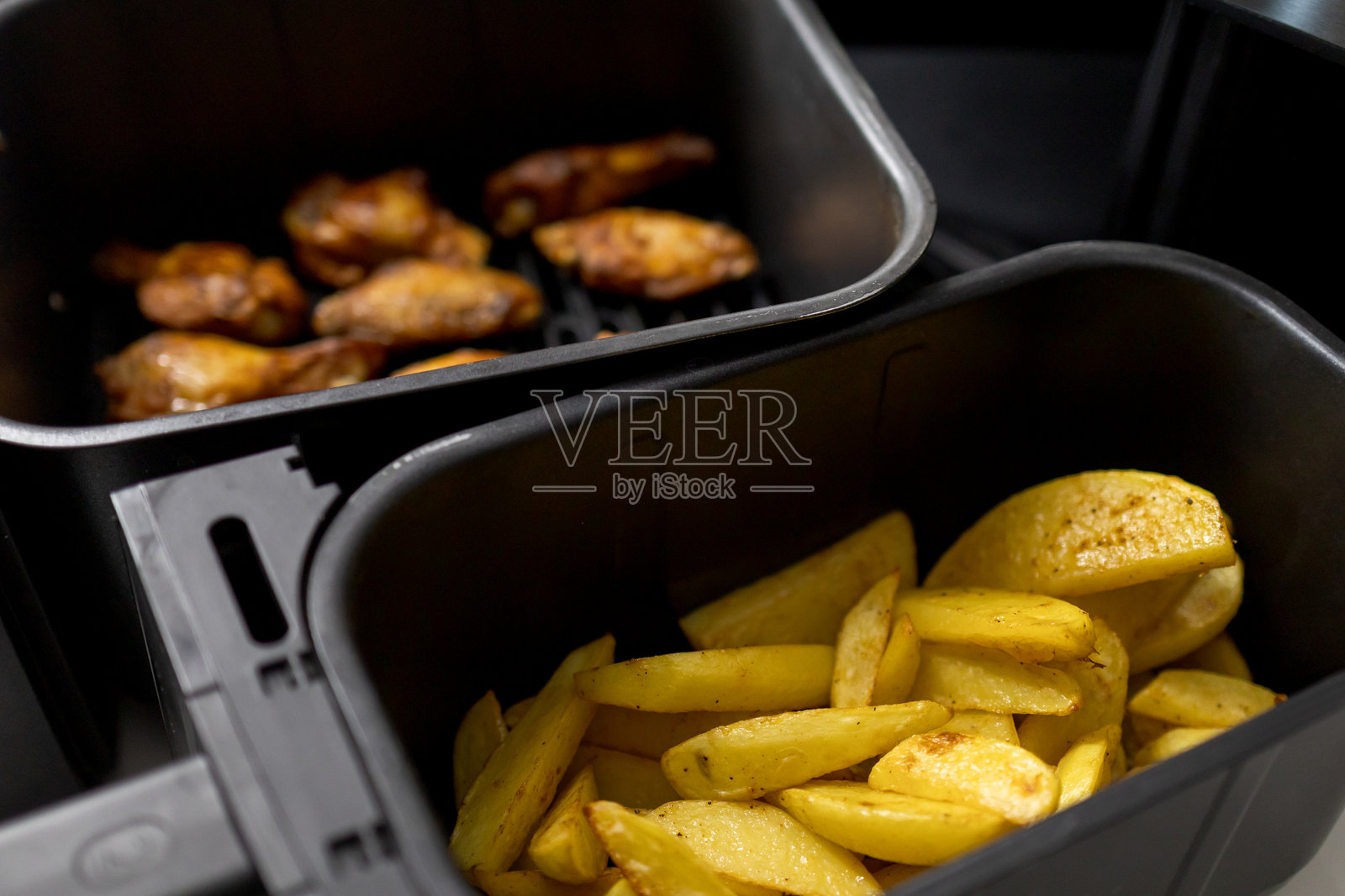 空气炸锅中烹饪的薯条（马铃薯楔）和鸡翅特写。照片摄影图片