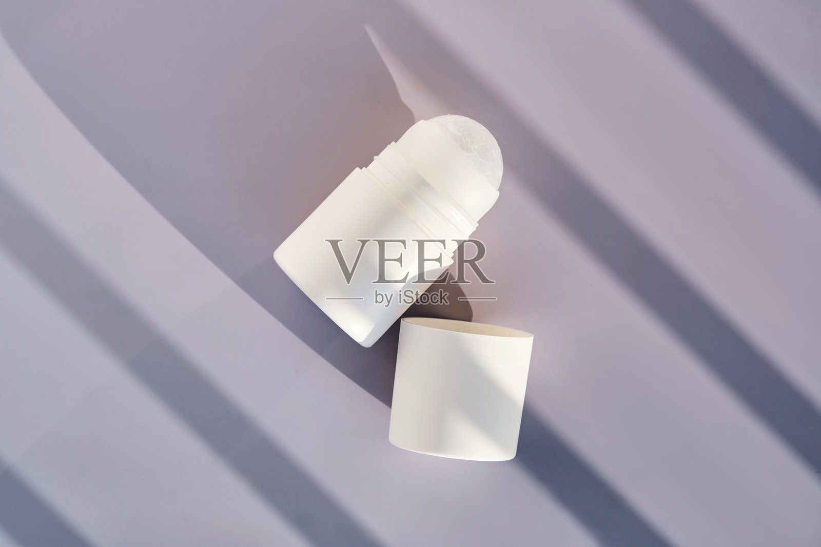 紫色背景上带有阴影条纹的滚珠香 deodorant。照片摄影图片
