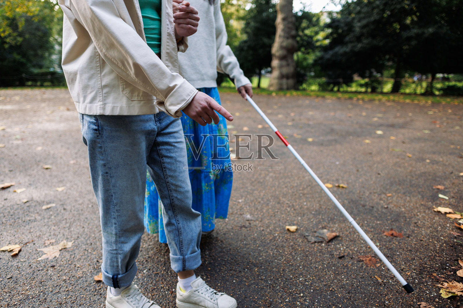 年轻男子在公园里引导一位使用白色手杖的盲人亚洲女性照片摄影图片