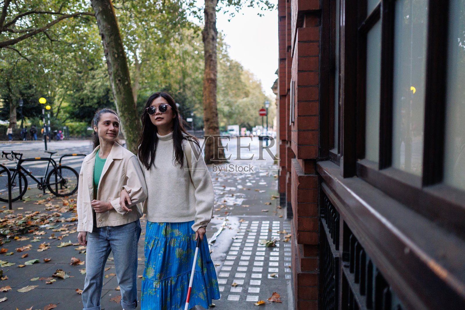 盲人女性牵着朋友的手臂在城市人行道上行走照片摄影图片