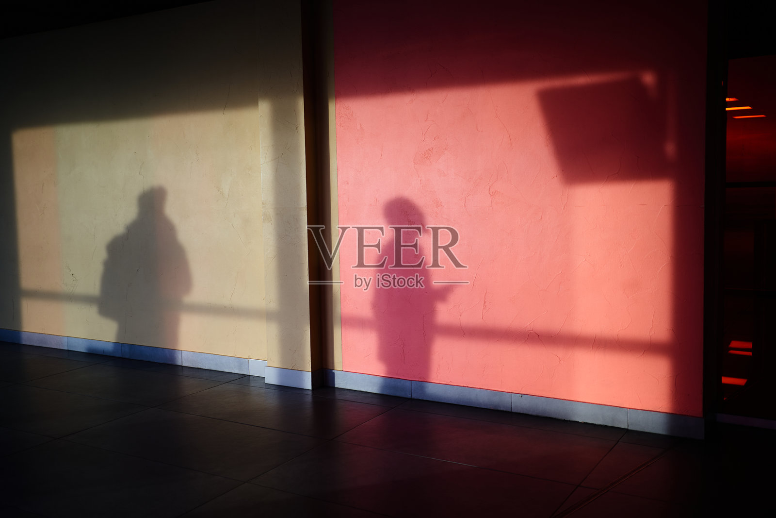 墙上的影子，一个男人在看出发屏幕。人们的轮廓在墙上反射。一个男人的影子在红色调的混凝土墙上。照片摄影图片