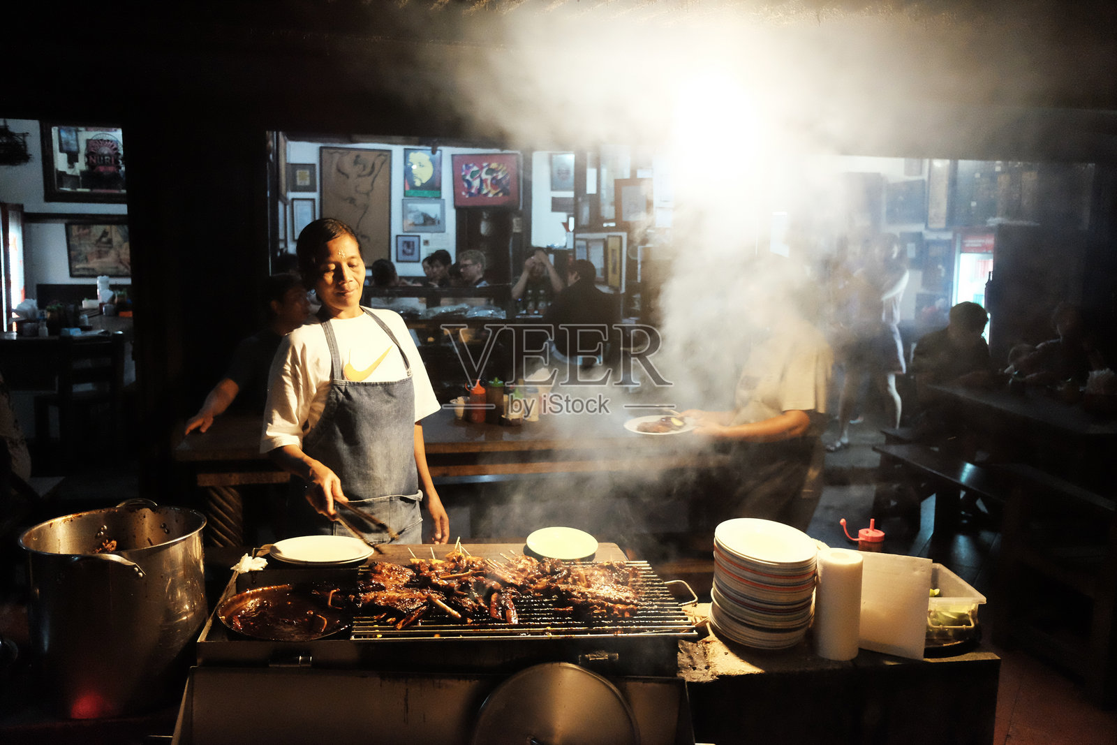巴厘岛的女摊贩在夜市步行街的当地餐厅里为顾客烤制烟熏猪肉。照片摄影图片