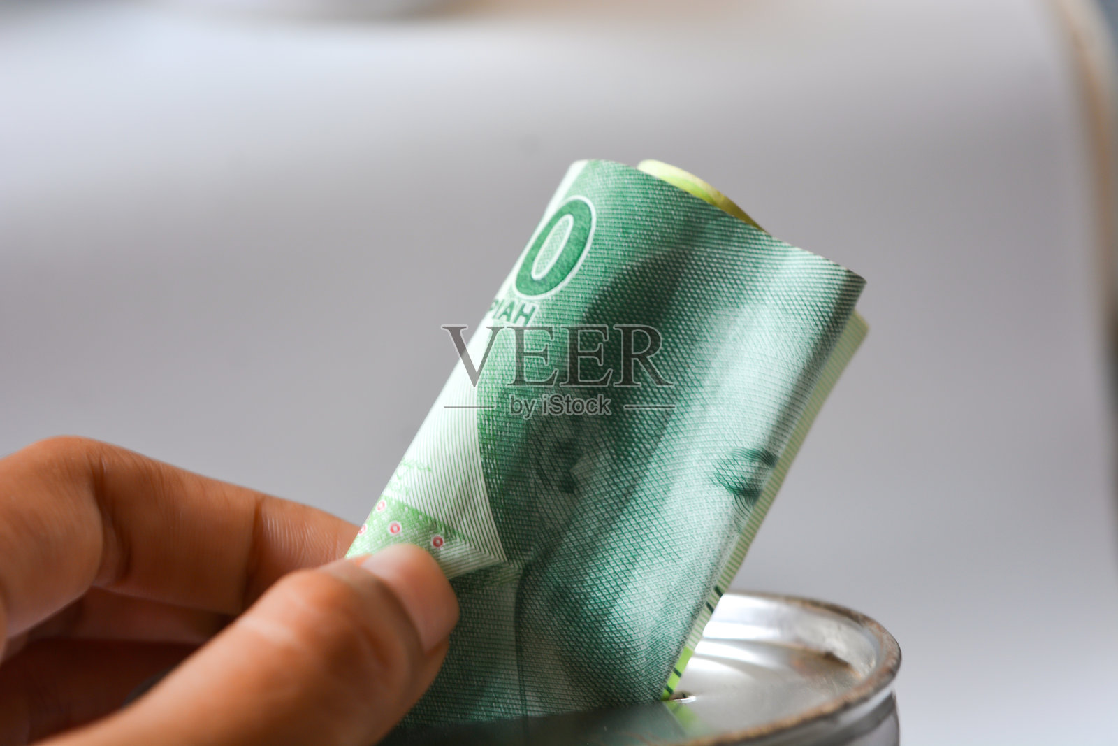 手将印尼盾放入传统印尼白色储蓄罐，背景为白色。特写，俯视角度。照片摄影图片