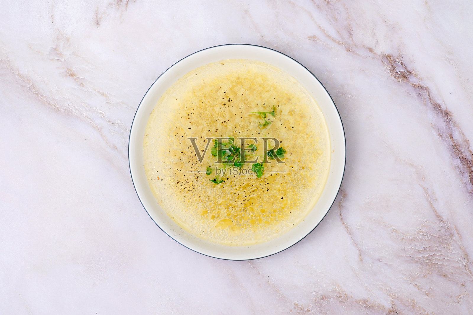 白色陶瓷碗中的即食鸡骨汤面，背景为白色大理石，点缀香菜。照片摄影图片