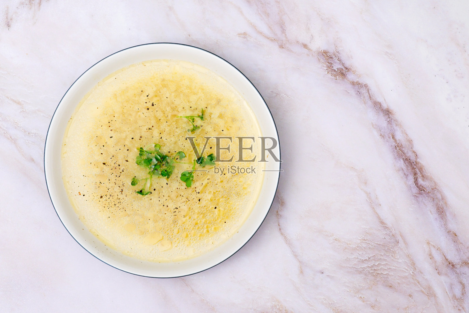 白色陶瓷碗中的即食鸡骨汤面，背景为白色大理石，点缀香菜。照片摄影图片