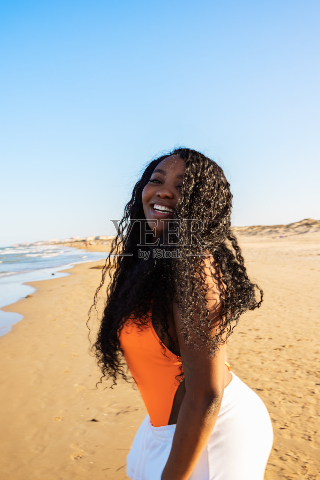 美丽的非裔美国女性穿着比基尼在热带海滩上。深肤色女性在海边微笑的肖像。棕发晒黑的女孩穿着泳装，享受并在沙滩上漫步。照片摄影图片