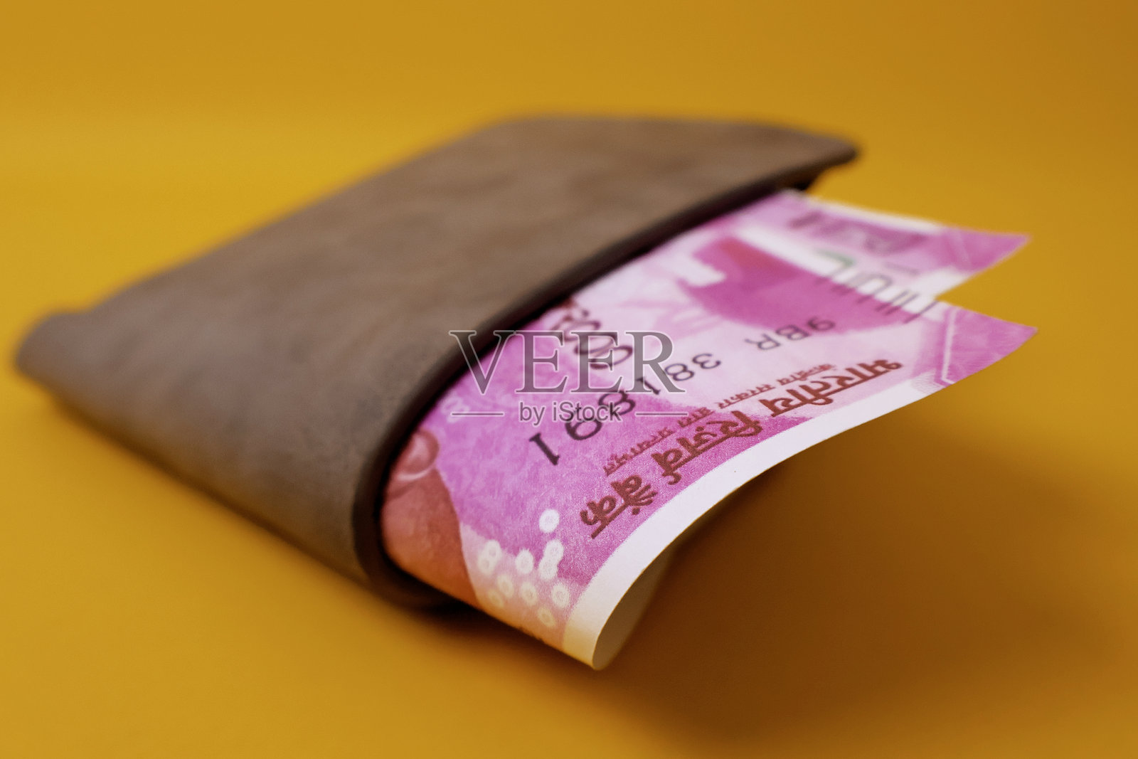 灰色皮革男士钱包中露出2000印度卢比钞票，背景为黄色。钱包里的印度卢比。照片摄影图片