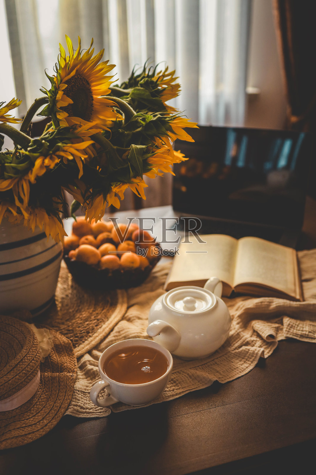 桌子上放着一杯茶、一本打开的书和一台笔记本电脑，夏天傍晚的氛围照片摄影图片