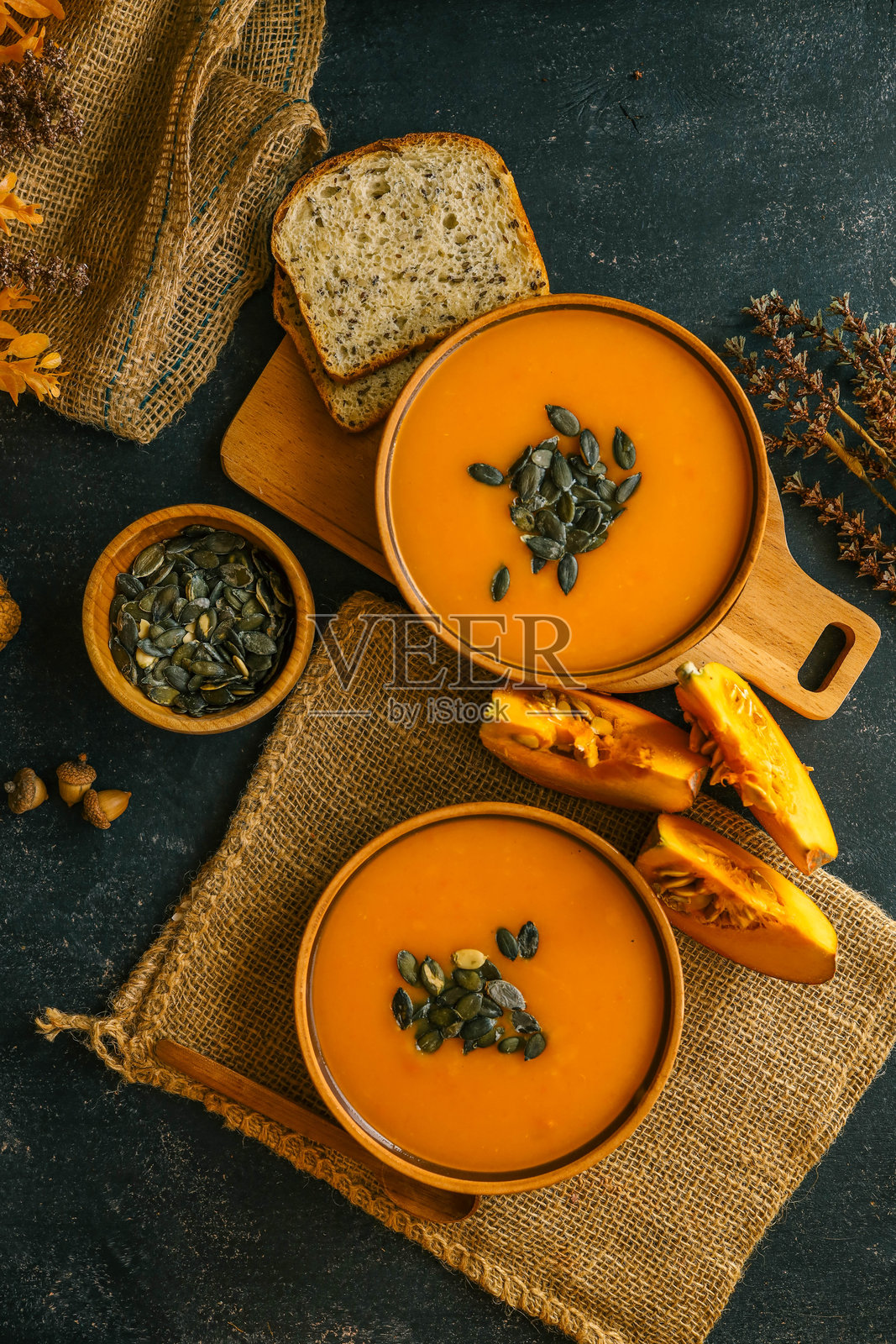 两碗南瓜泥汤，配有肉丸、南瓜籽和一枝迷迭香，横放在深色背景上。照片摄影图片