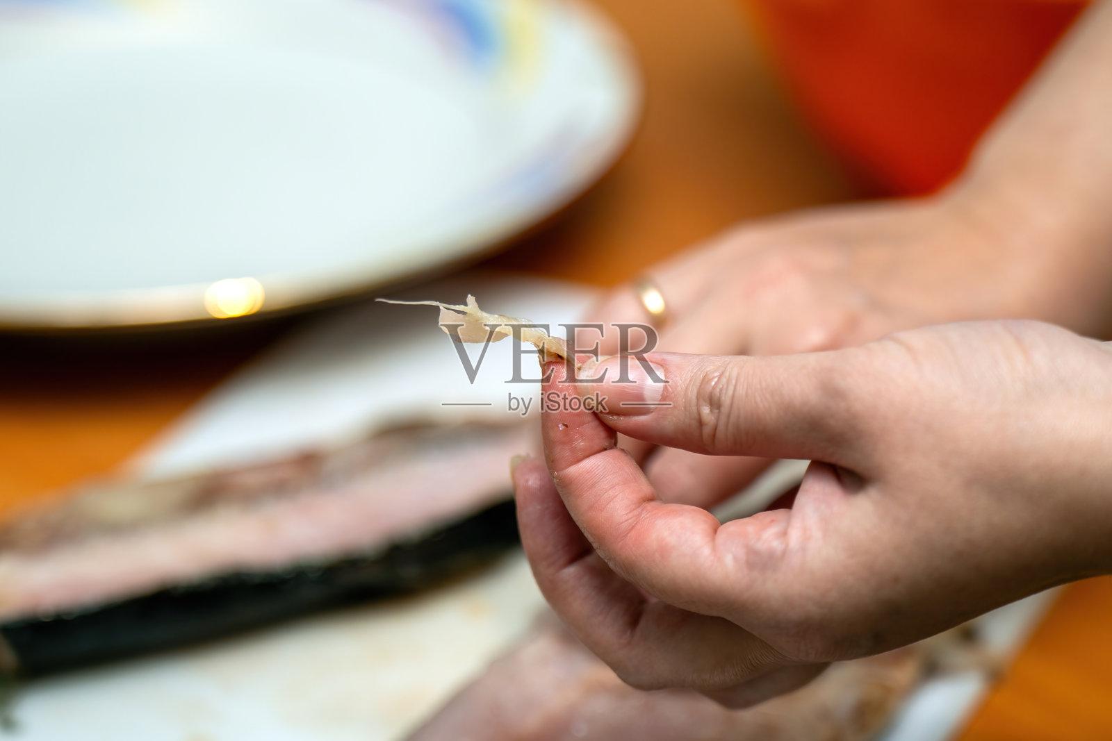 女人的手轻柔地握着一根鱼骨，展示了鱼片制作的细致过程以及与烹饪工艺的联系。照片摄影图片