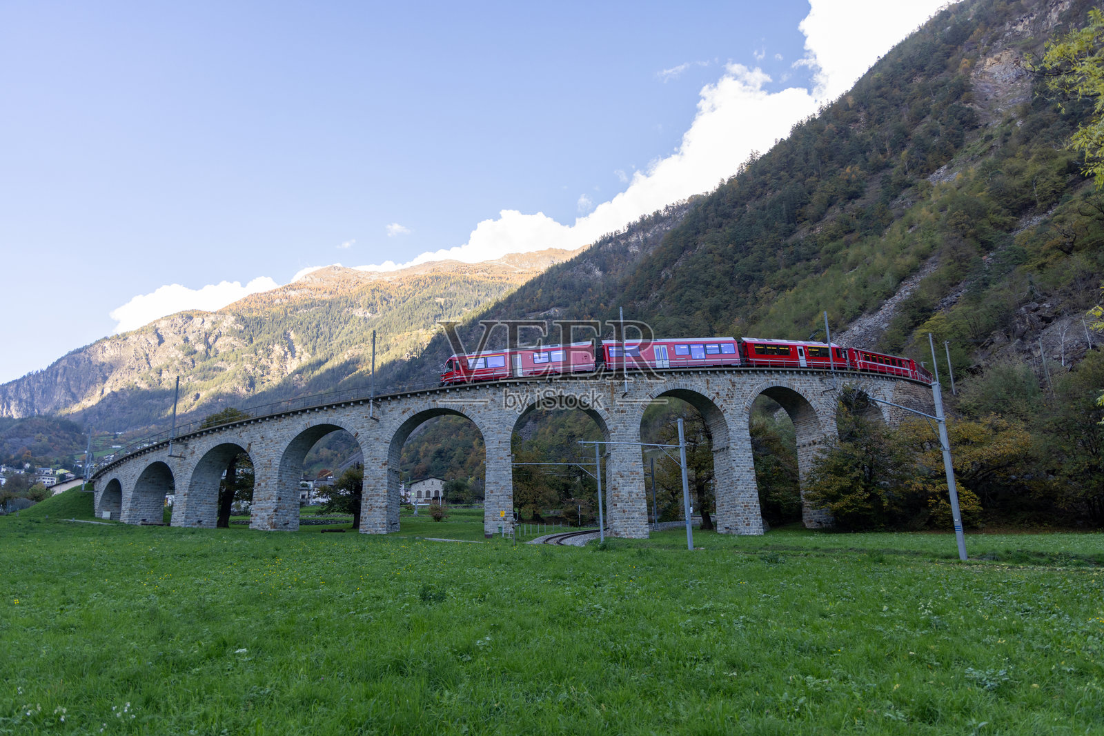 红色火车穿越山谷中的石拱桥照片摄影图片
