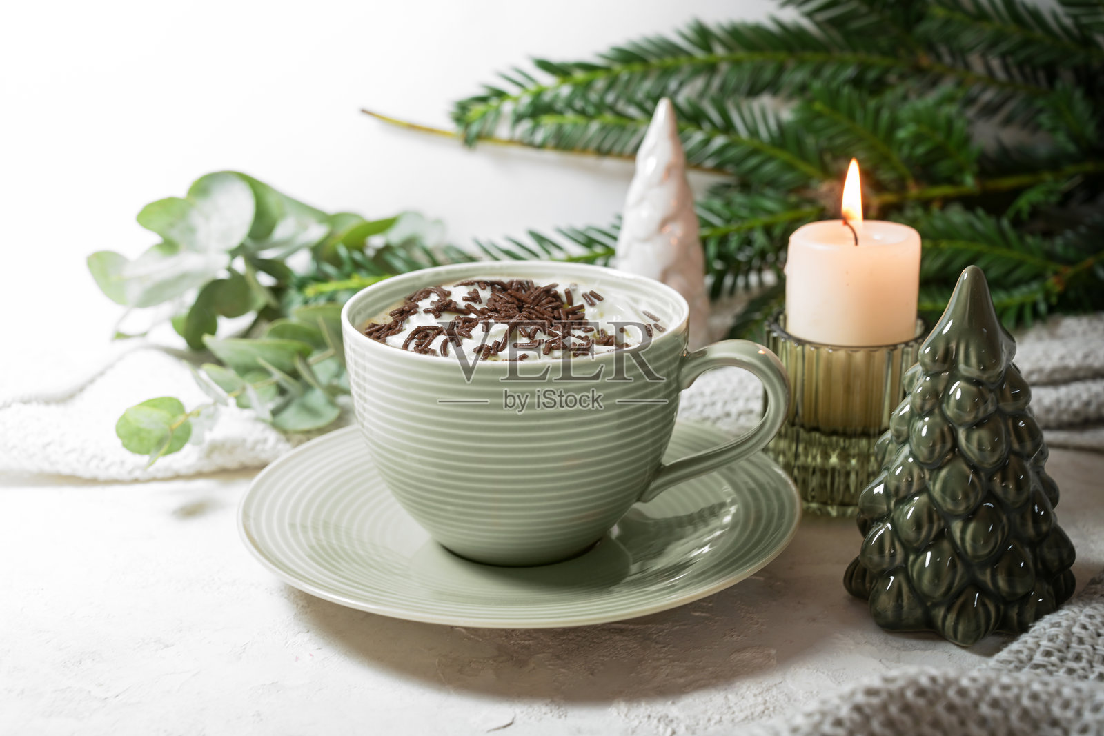 绿色杯子里装着热巧克力和奶油，旁边有蜡烛、树枝和圣诞装饰，背景明亮，适合在家享用的甜饮，留白，聚焦选择。照片摄影图片