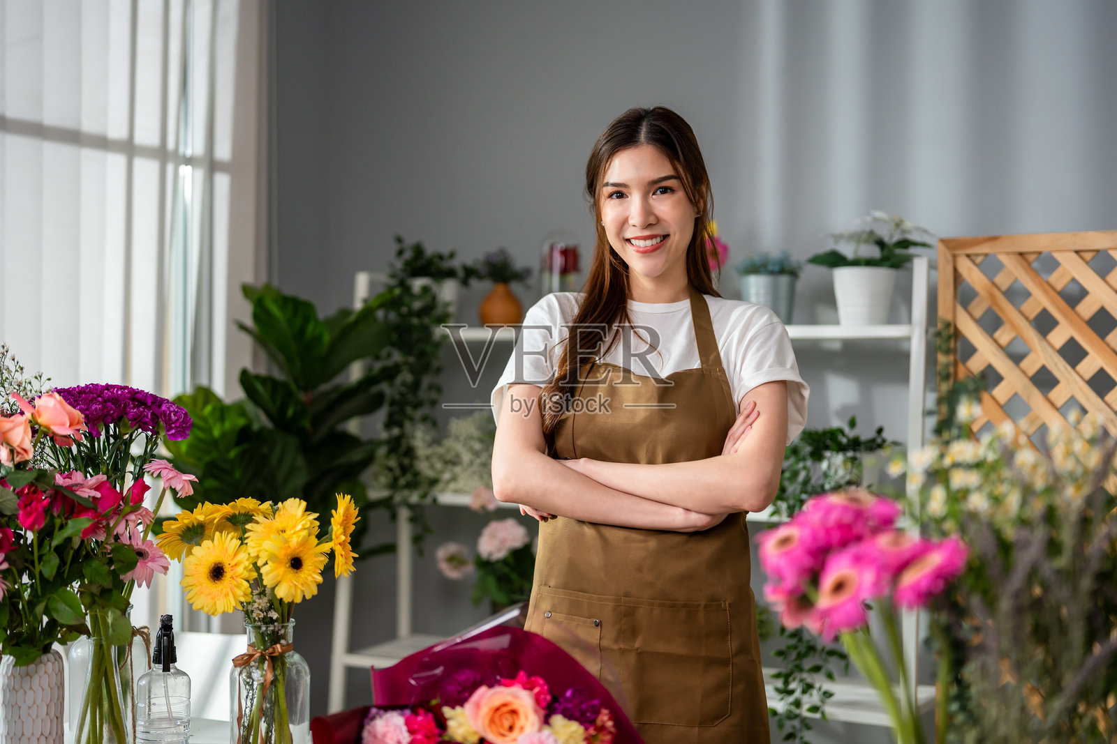 花店女花匠在完成美丽的花束。迷人的女性小企业主对着镜头微笑，同时为顾客包装花卉礼品。照片摄影图片
