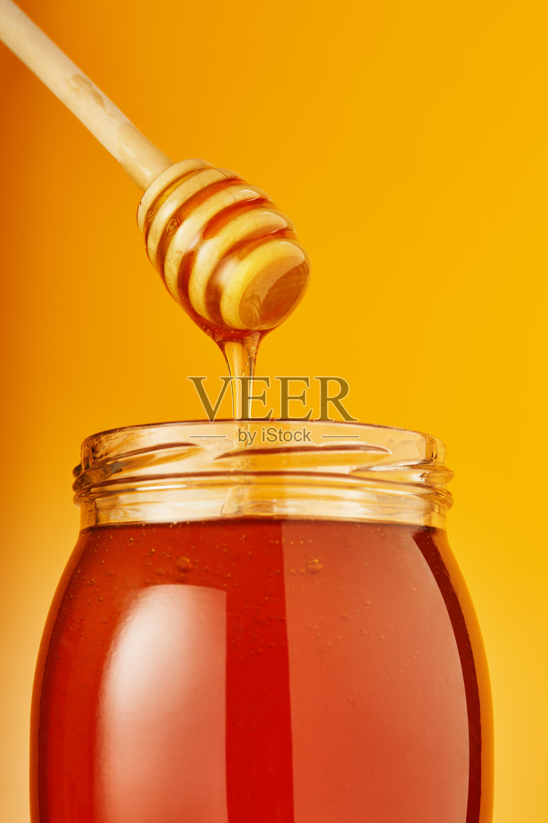 蜂蜜从木制蜜杖滴入罐子中照片摄影图片