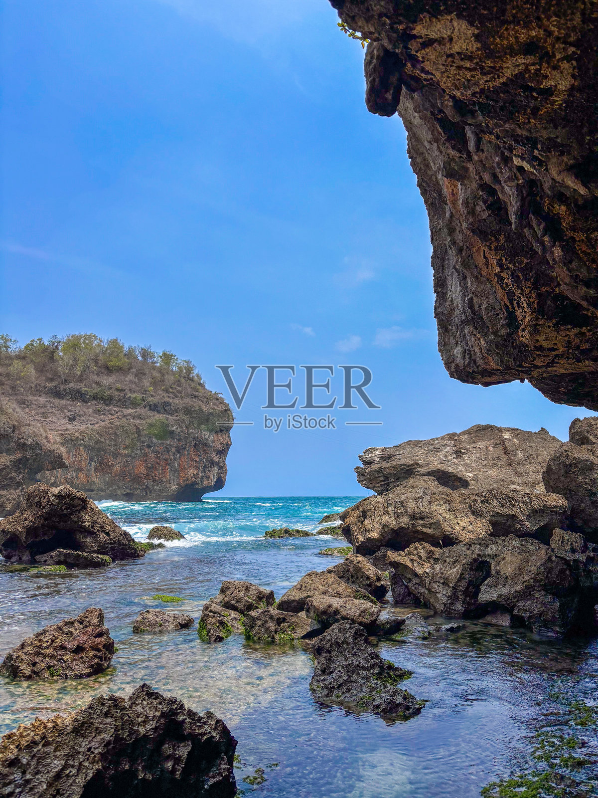 一个岩石海滩，前面有一小片平静的水域，背后是悬崖。水面平静，天空晴朗。照片摄影图片