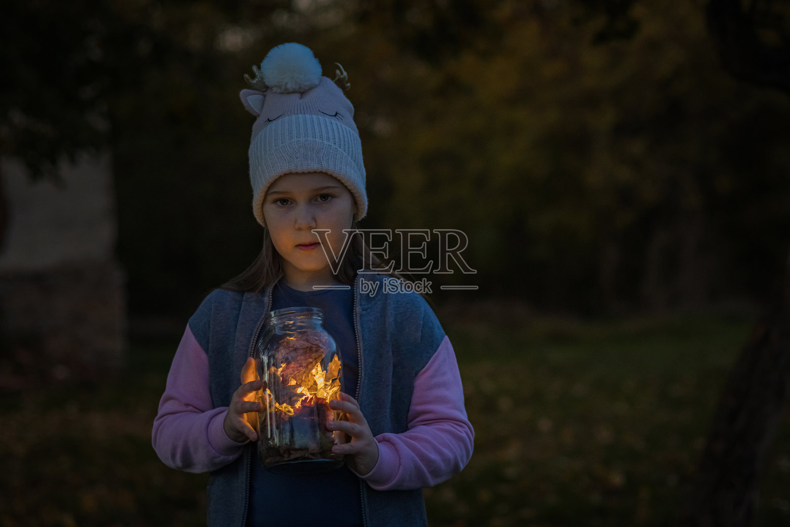美丽的小女孩在后院玩耍，手中拿着装有灯光的罐子。圣诞节的灯光照亮了她快乐的脸庞。照片摄影图片