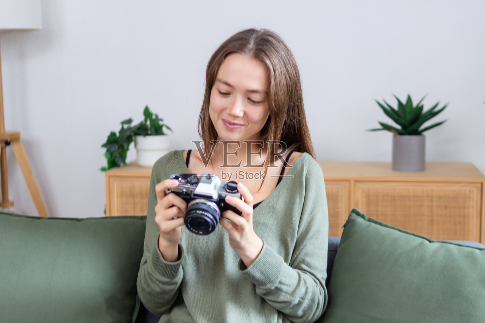 年轻女性在家中微笑着拿着一台复古相机，查看照片。照片摄影图片