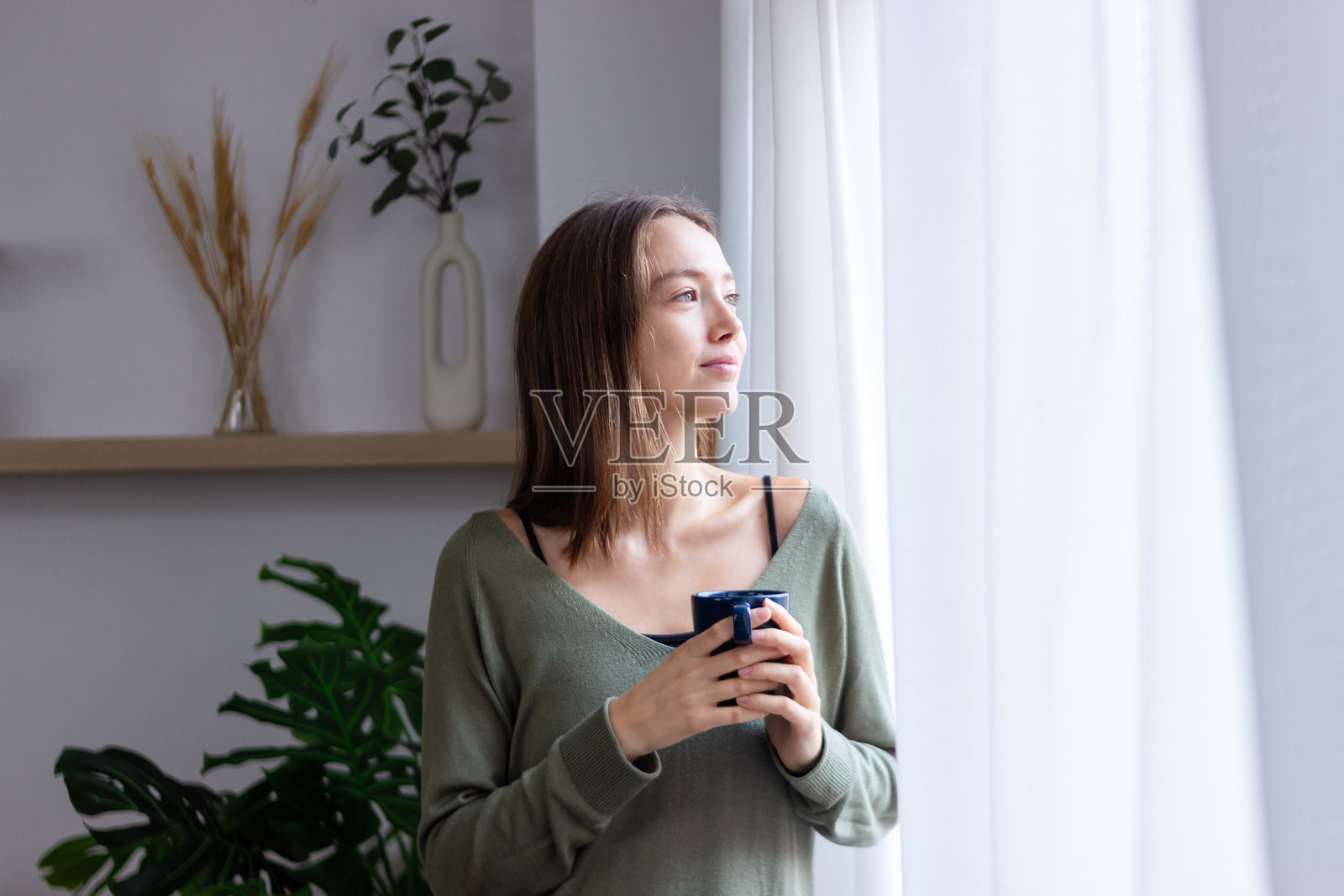 年轻女性在家喝咖啡，望着窗外照片摄影图片